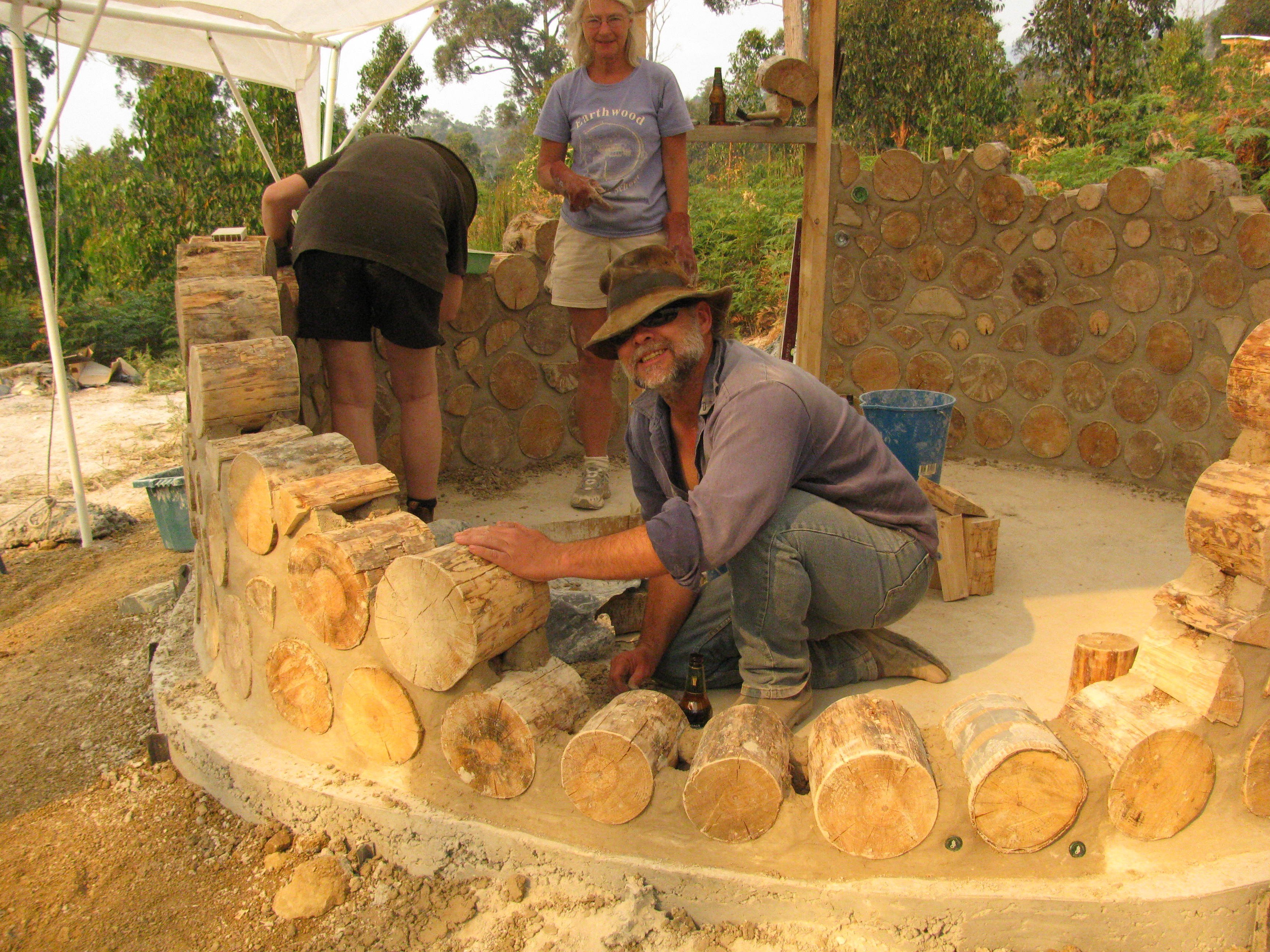 At a cordwood masonry construction workshop in Tasmania, Australia, Jaki looks on as a student sets a log-end for a cordwood sauna.